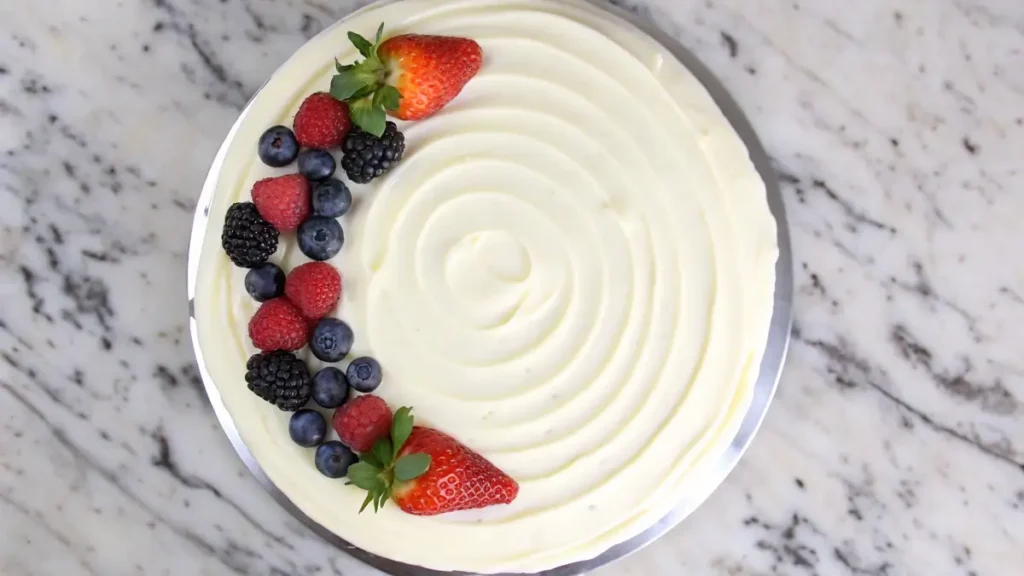 Chantilly Cake: Elevate Your Dessert Game Top view of a cake with smooth whipped cream frosting, garnished with fresh strawberries, blueberries, raspberries, and blackberries.